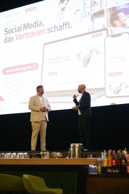 Patrick Rettler-Koch bei einem Vortrag auf der ERGO Bühne vor der Projektion der Website